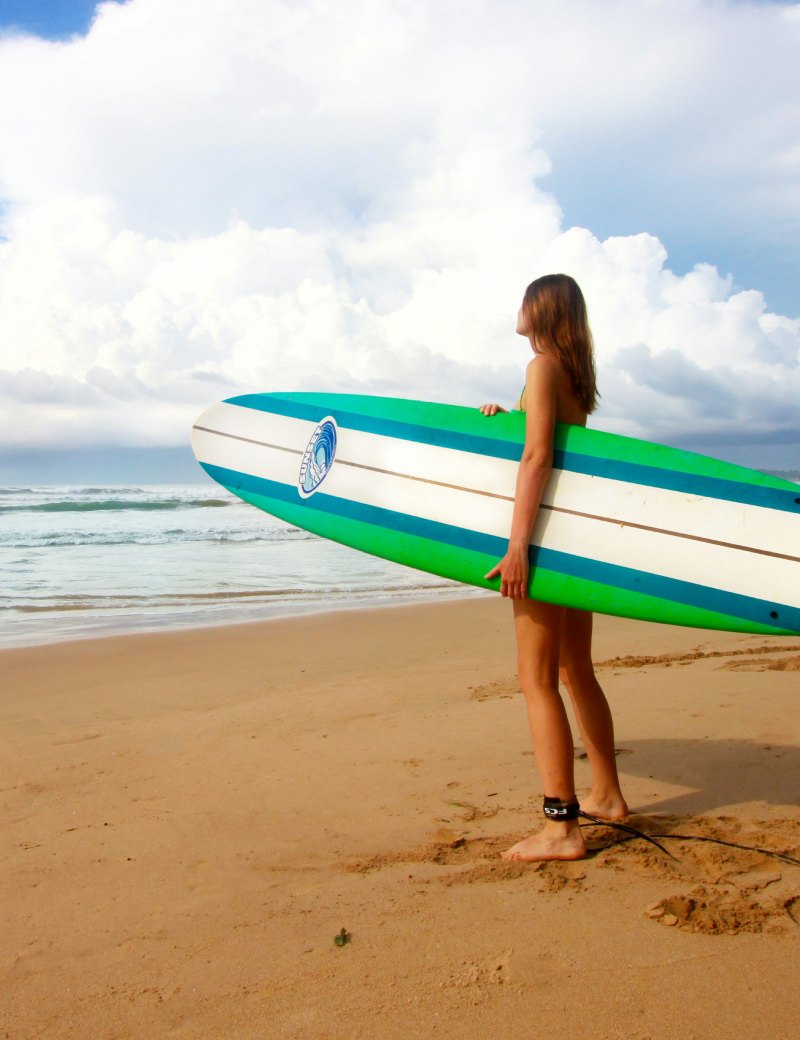 Woman holding a surfboard on a sandy beach in Weligama, enjoying surf in Sri Lanka with ocean waves and cloudy sky in the background
